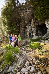 A family with a dog hiking in front of a cave.
