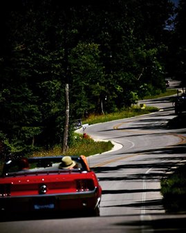 Two people driving in a red car down a winding road.
