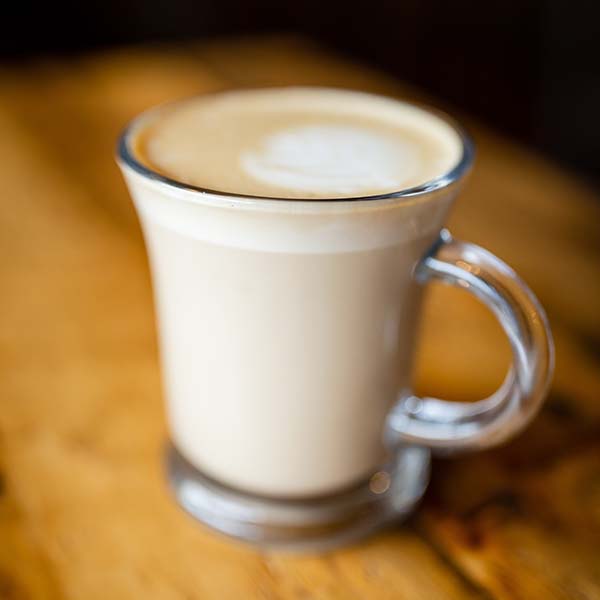 A warm latte in a clear glass sits on an artisan wood table.