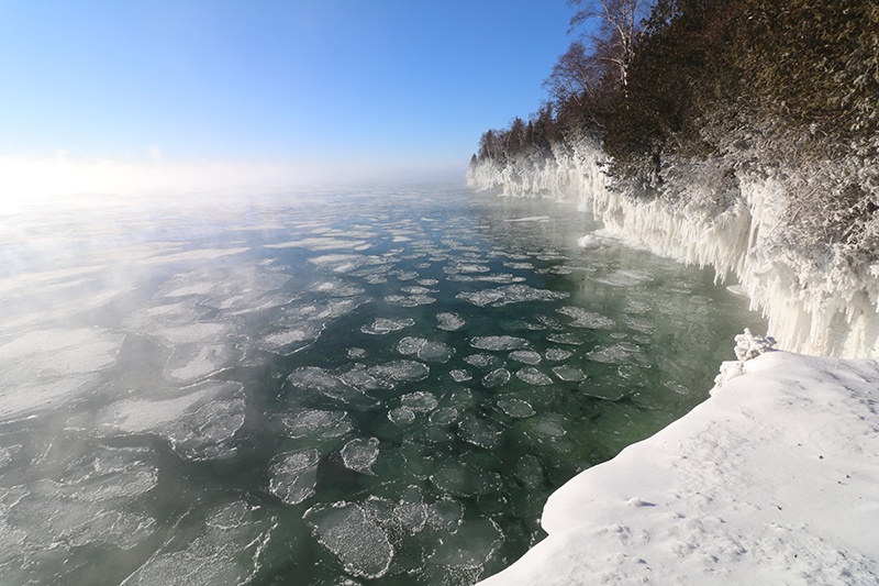Snow-covered cliffs at the edge of the lake with chunks of floating ice