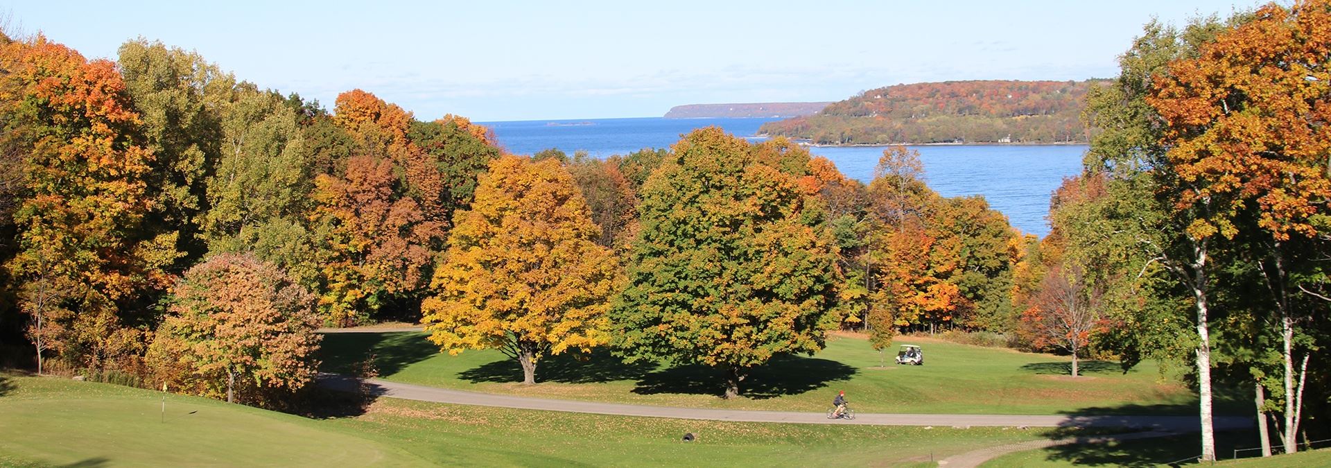 A golf course surrounded by colorful trees and the lake in the distance.