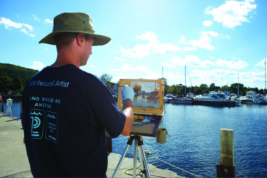 A man paints the marina and lake scene in front of him.