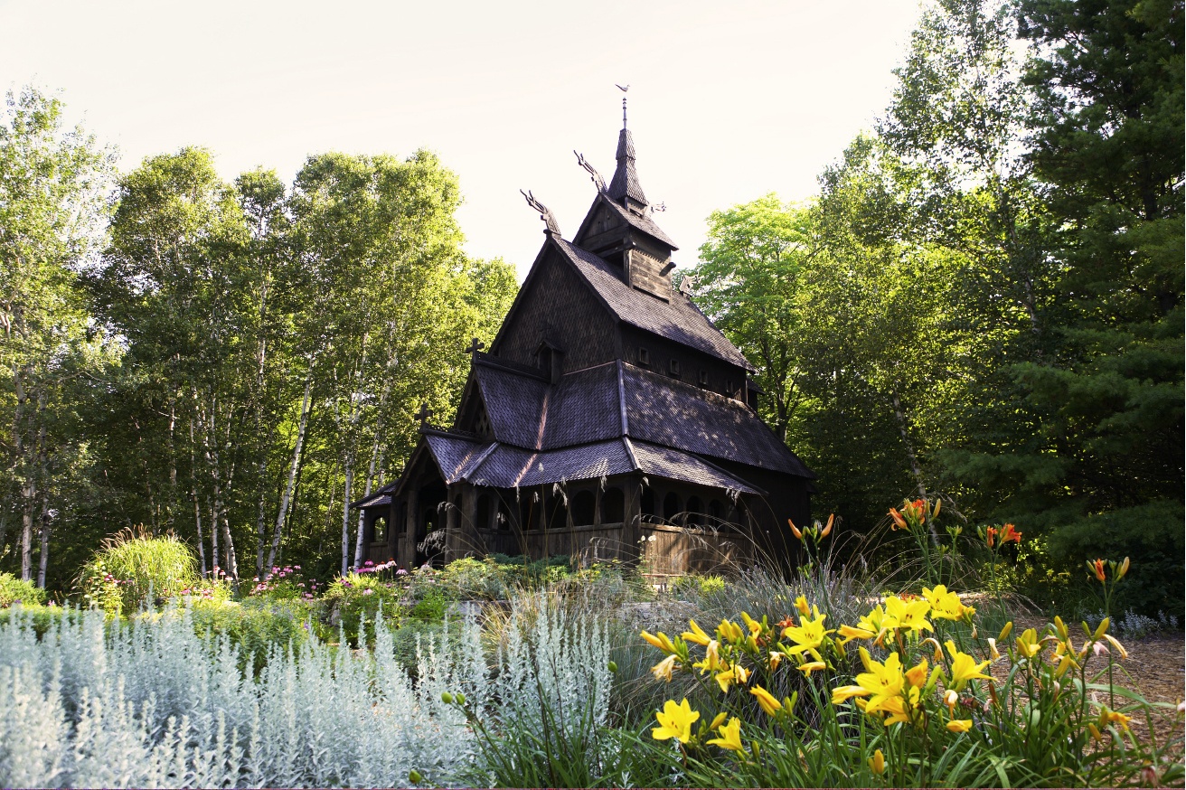 Ornate wooden building surrounded by flowers and trees.