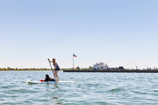 A woman on a standup paddleboard with a dog lying on it.