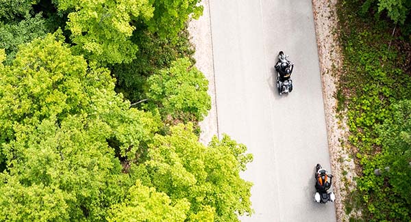 Aerial view of motorcycles driving on a tree-lined road.