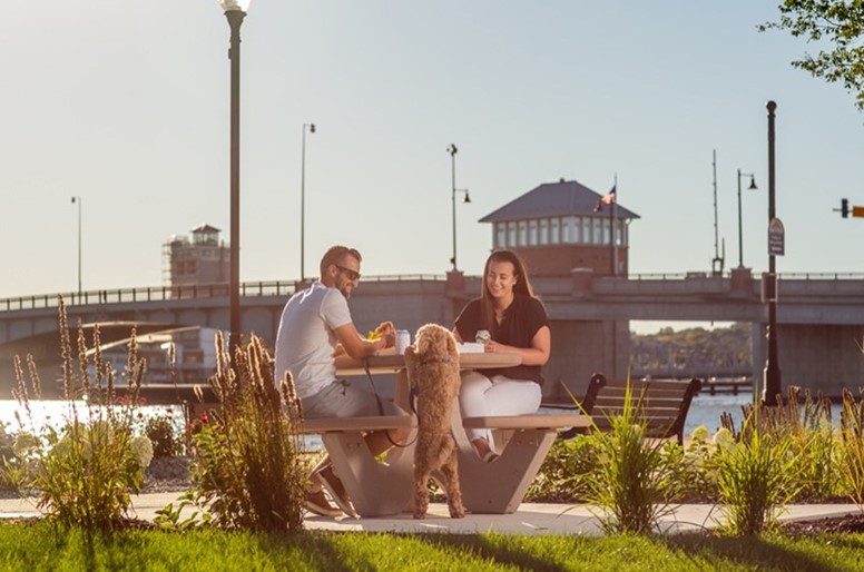 A couple and their dog sitting a picnic table in a park.