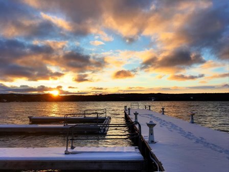 The sun setting over the lake beyond a snowy pier.
