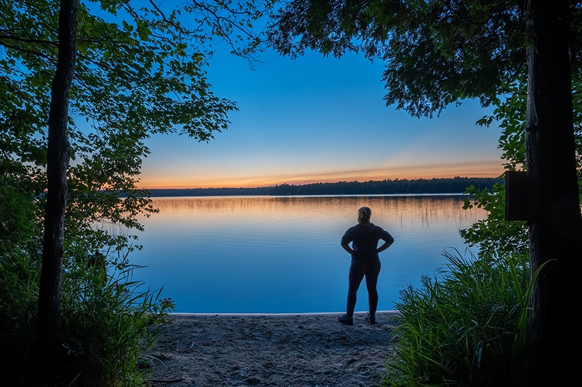 A woman stands aside Europe Lake at Newport State Park during a brilliant sunset.