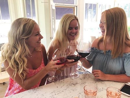 Three women toasting with glasses of red wine.