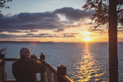 A person bundled up looking at the sunset over the lake.