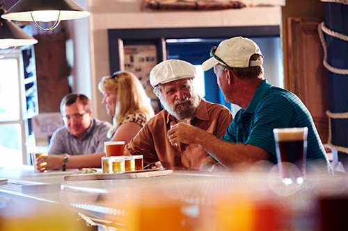 Two men sip beers at a bar with a nautical decor.