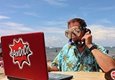 A man wearing diving goggles sitting in front of a laptop on the phone