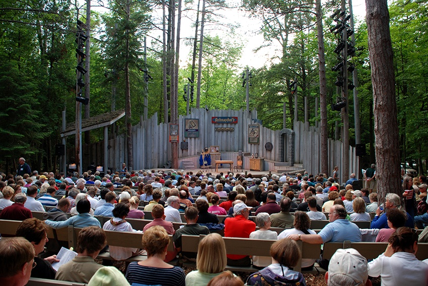 A crowd watches a performance at an outdoor forest theater