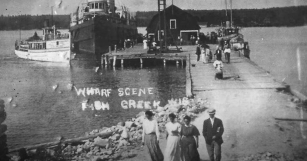 Vintage photo of early residents in front a dock and passenger boats