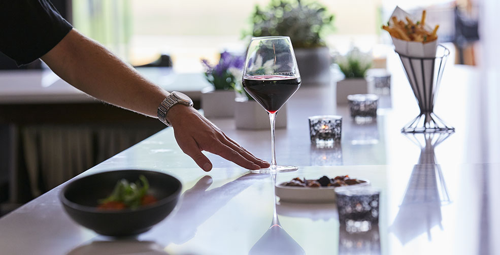 A person's hand touching a glass of red wine.