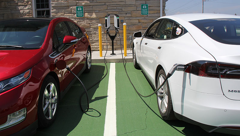 Close up of two cars parked at an electric charging station.