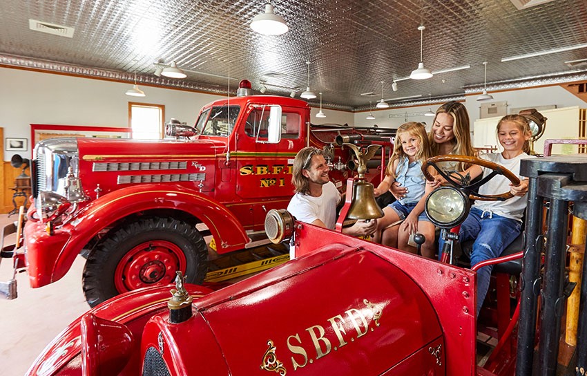 A family sitting in an old fire truck in a museum.