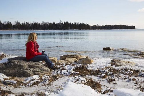 A woman sitting on a rock at the snow-covered lakefront.