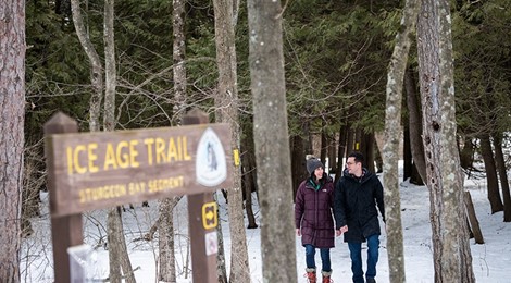 Couple walking through the woods in the snow near an Ice Age Trail sign