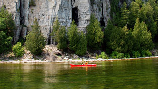 A kayaker paddling in front of a large cliff.