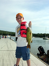 A young kid holding up a fish he caught.