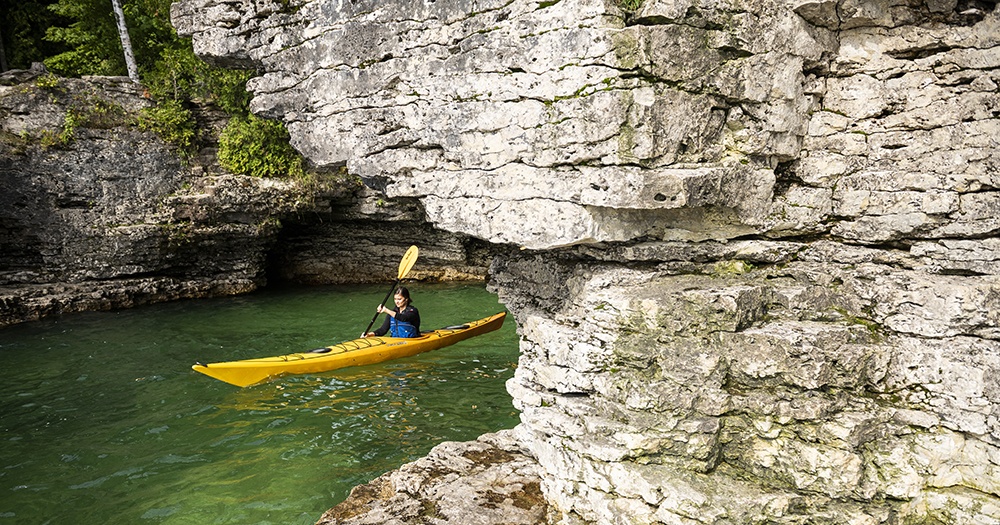 A woman kayaking among caves and rock formations.