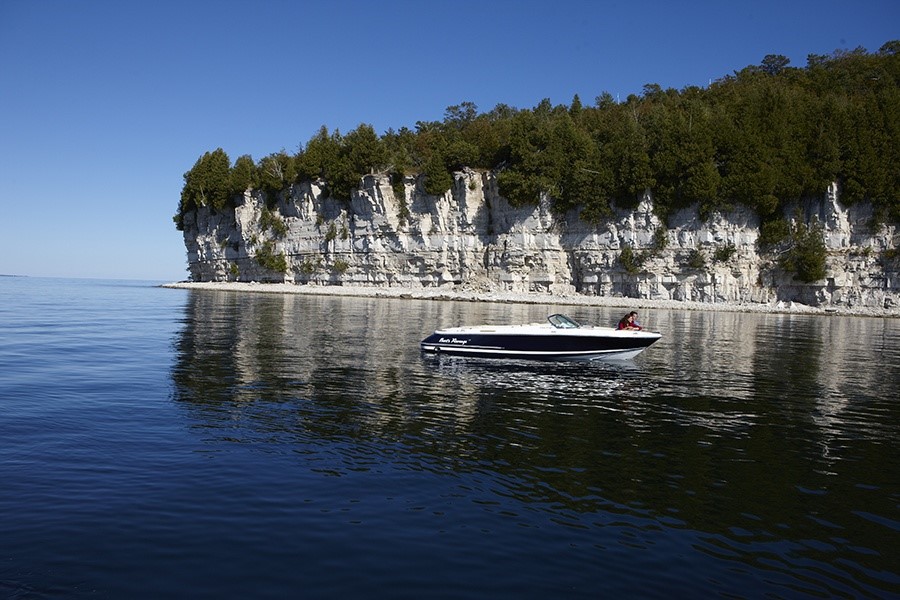 A boat on the lake with white tree-lined cliffs in the distance.