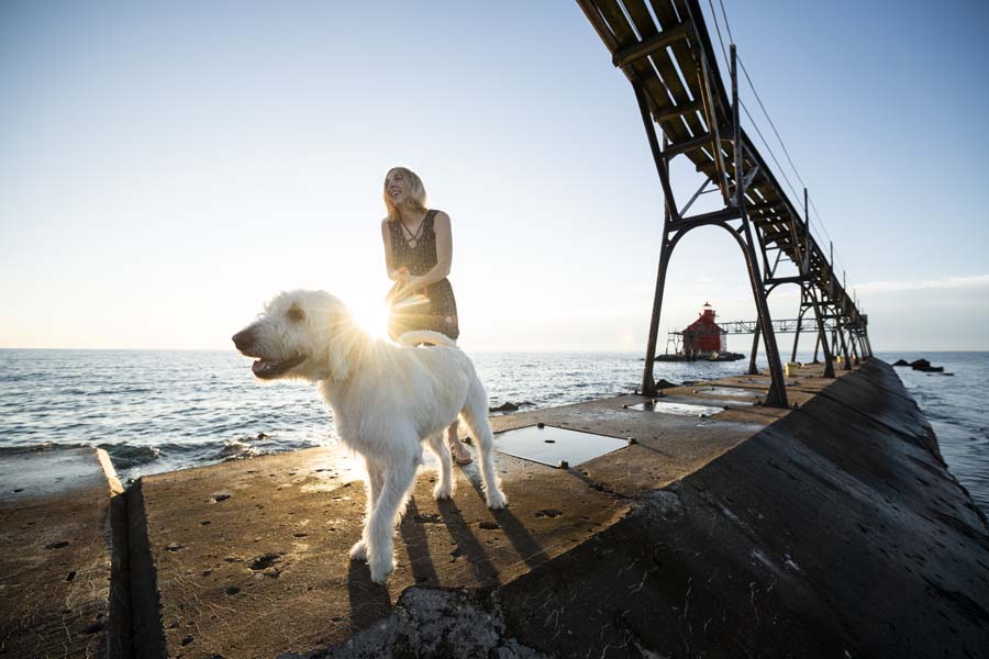 A woman walks her dog near a lighthouse.