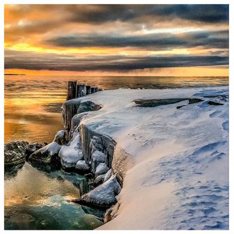 Snow-covered rocks on the lakeshore at sunset.