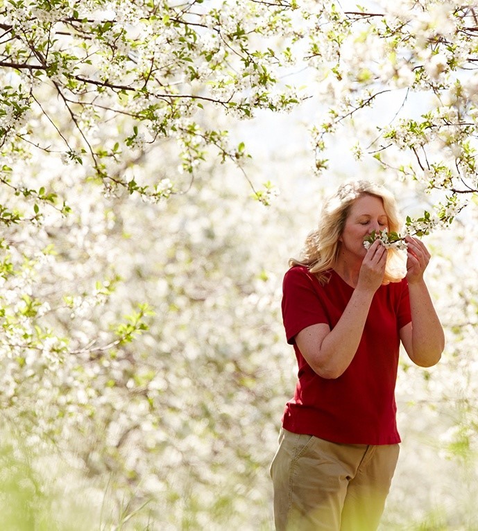 A woman smelling flower blossoms on a tree.
