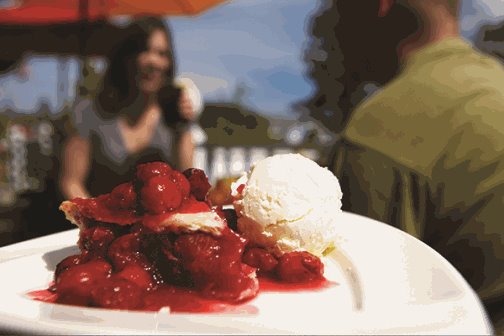 A plate of cherry pie with ice cream with people dining in the background.
