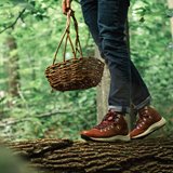 Closeup of a person walking across a fallen log holding a basket.