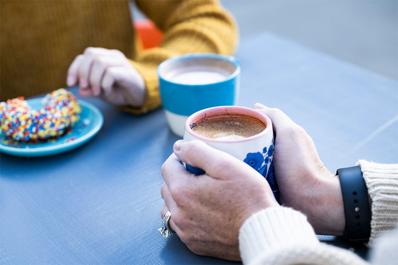 A woman cups a cup of coffee in her hands when across from her a person