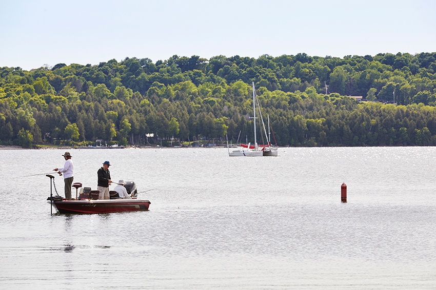 The Door County Fishing Guide Men fish from a motor boat with a sailboat in the background