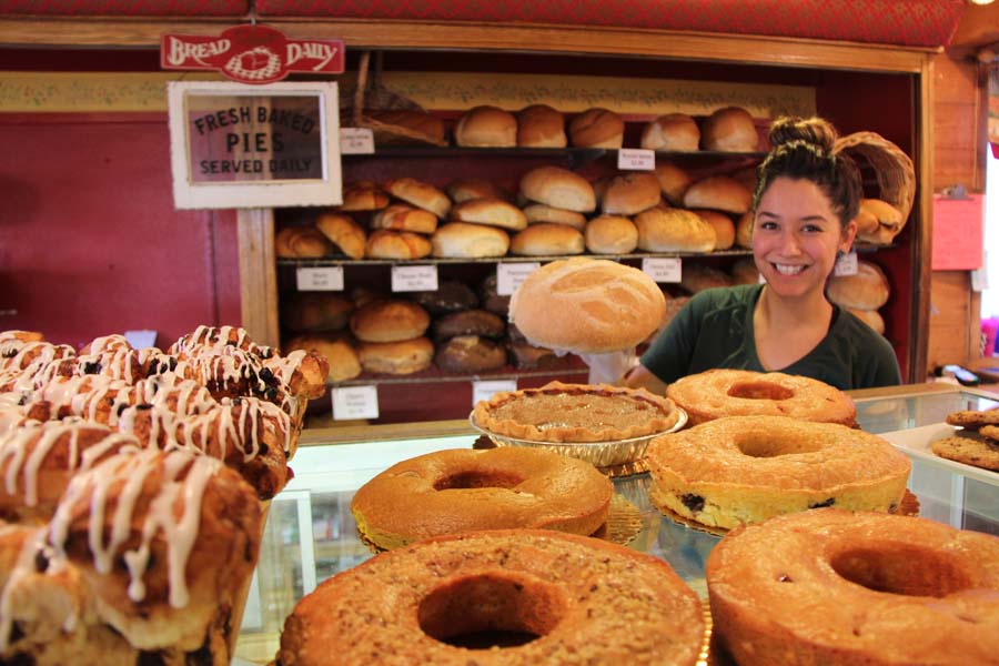 A smiling employee looks over cakes, muffins, and breads at Scaturo
