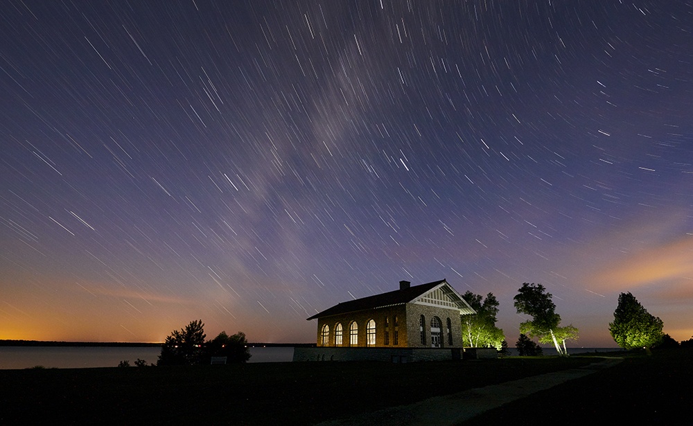 Stargazing: 300 Billion Reasons to Visit A remote boathouse illuminated by the purples and oranges of the Northern Lights