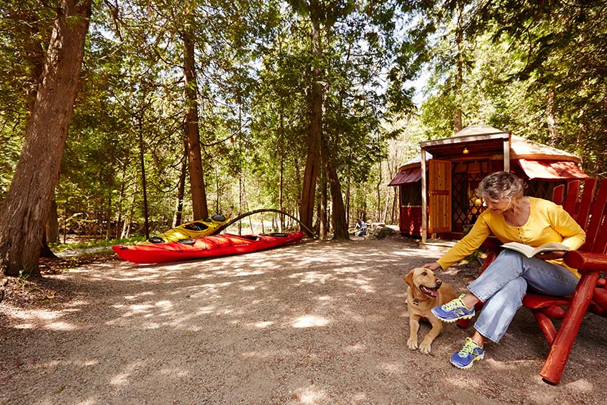 Cabins A woman and her dog sitting outside a cabin with a kayak in the background.