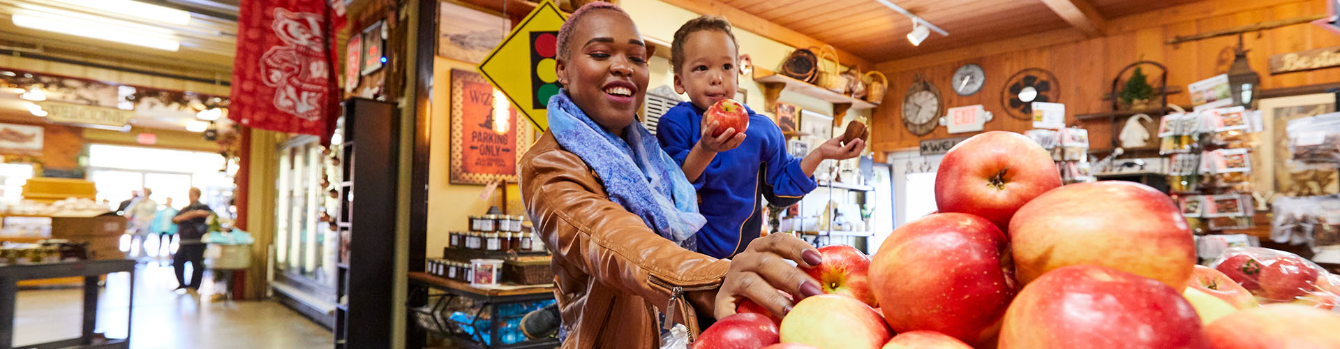 Markets & Specialty Foods A woman holding her child while picking an apple at a market