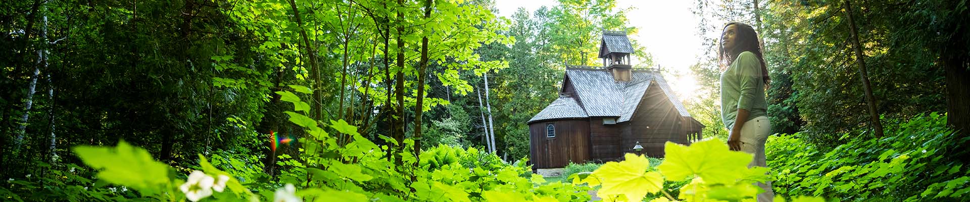 3-Day Spiritual Journey A woman immersed in nature and sunlight near a wooden building.