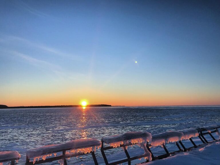 Iced over pier railings with a sunset over the lake in the background