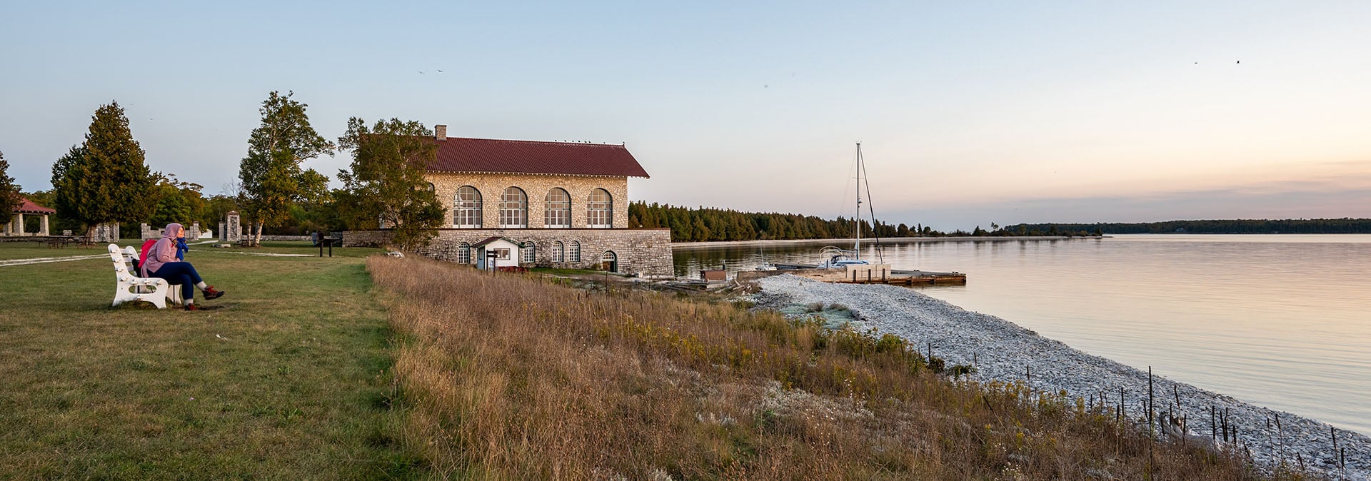 Parks in Door County People sitting on a bench looking out at the sunsetting over the lake with the stone boathouse in the background