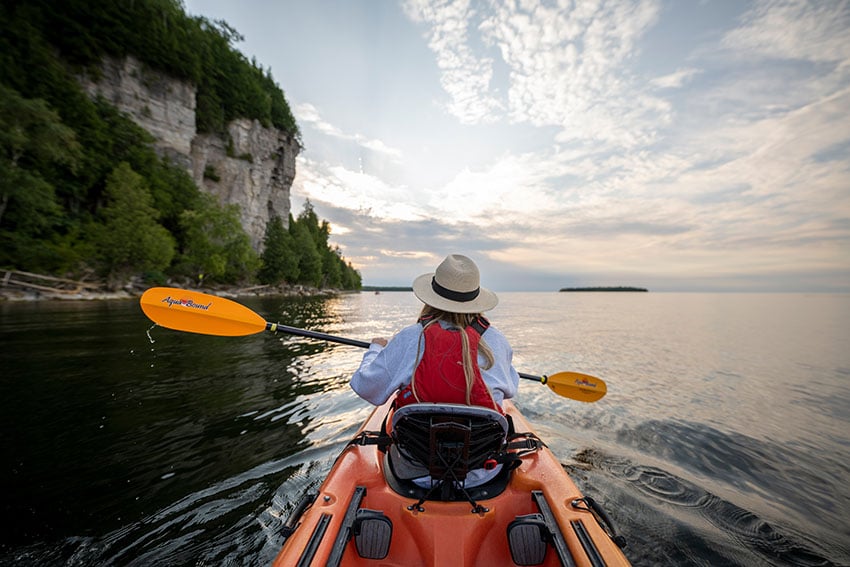 Parks in Door County Point of view from the back of a kayak looking at the front person in still water by the cliffs